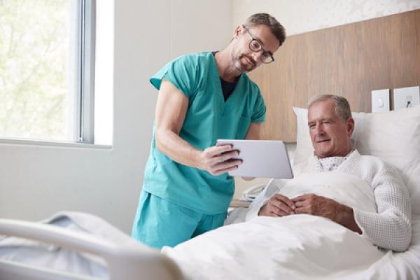 A doctor shows a patient who is laying in bed a chart