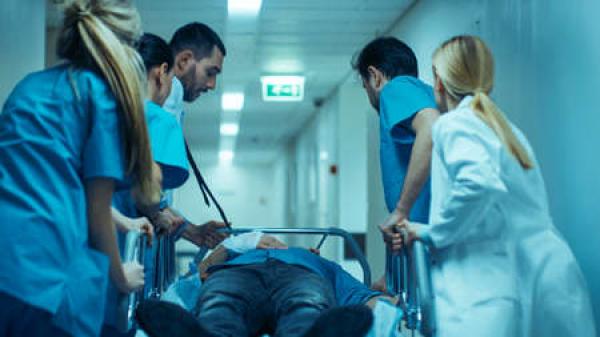 A group of doctors and nurses take a patient down a hall on a gurney